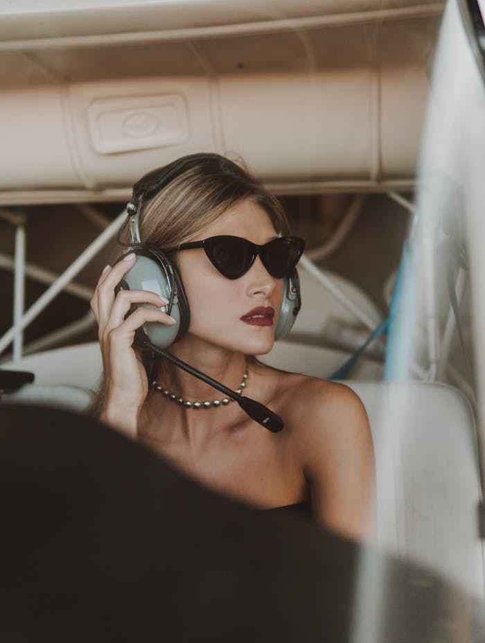 Stylish female pilot with sunglasses and headset inside airplane cockpit, vintage vibe.