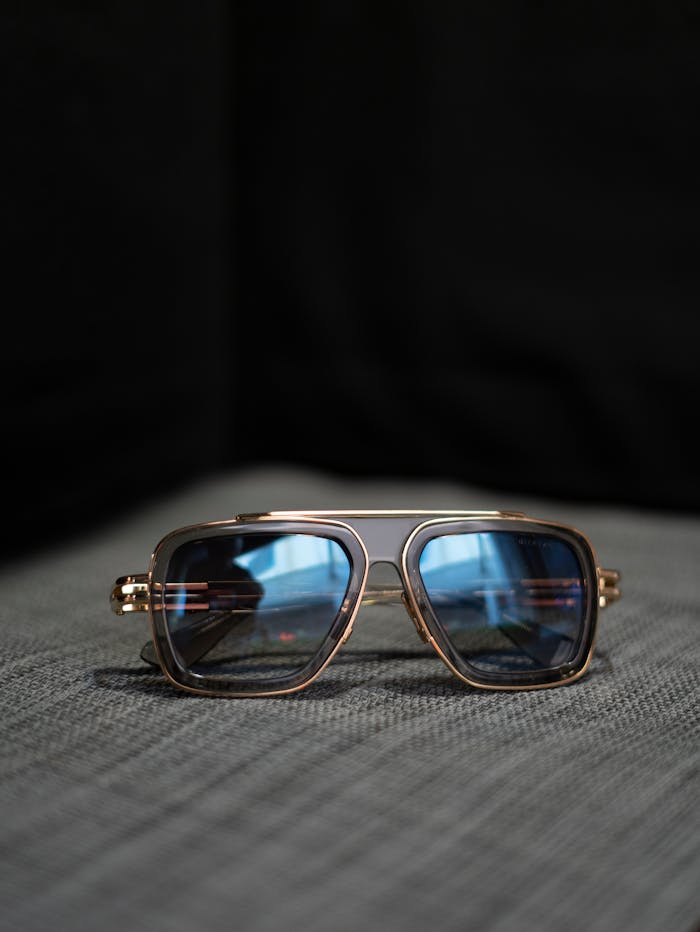 Elegant aviator sunglasses with blue lenses and gold frame on a textured grey surface.